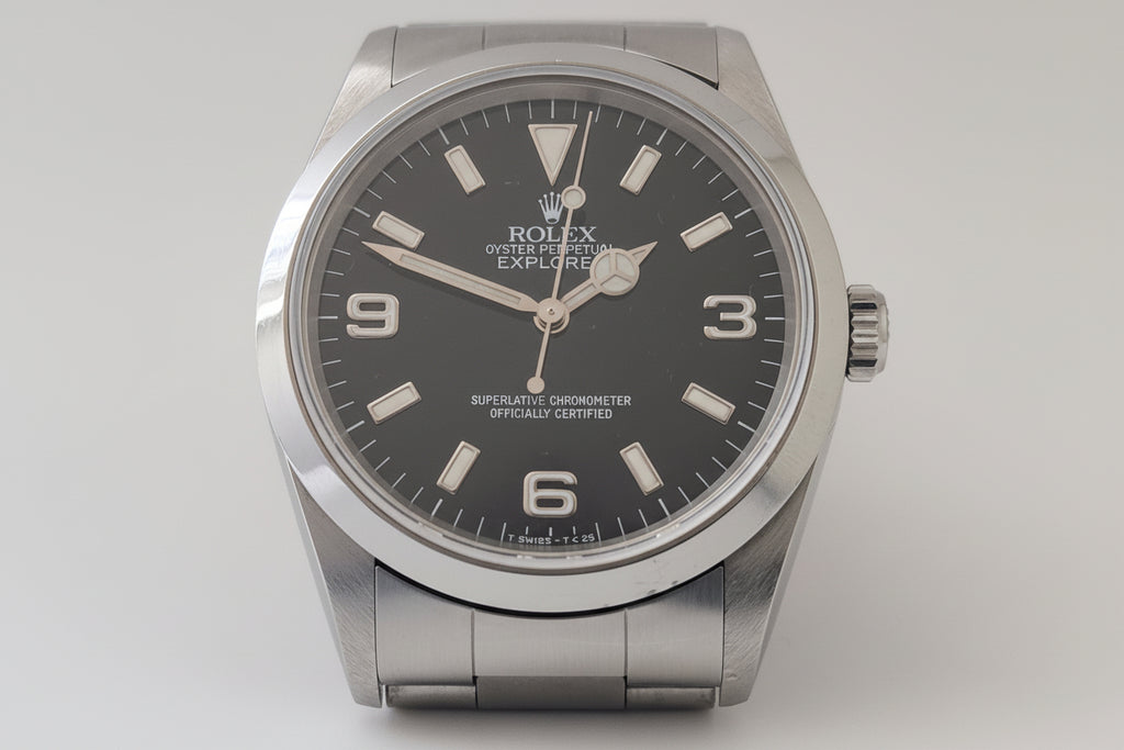 Rolex watch with black dial and silver case on a light gray background