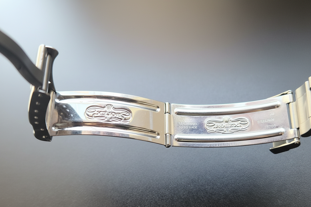 Close-up of a silver watch band with brand logo on a reflective surface